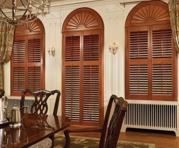 Shutters Dining room with wooden table and chairs, featuring three arched windows with wooden shutters and drapes.